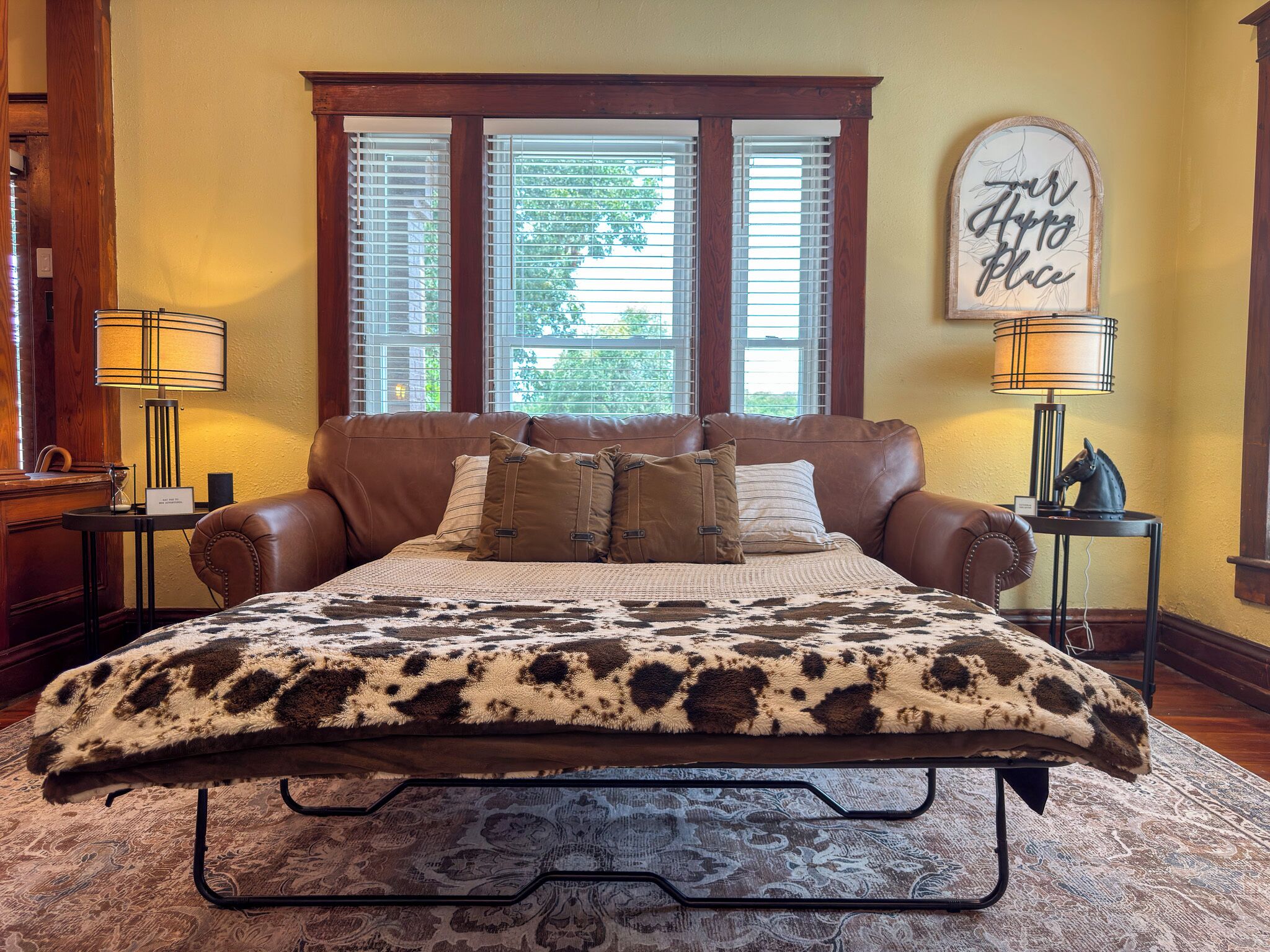 A bedroom with a large bed, two bedside tables, a wall clock, and a window with blinds.