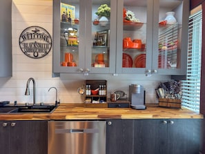 A kitchen with a stainless steel dishwasher, a coffee machine, and a wooden countertop.