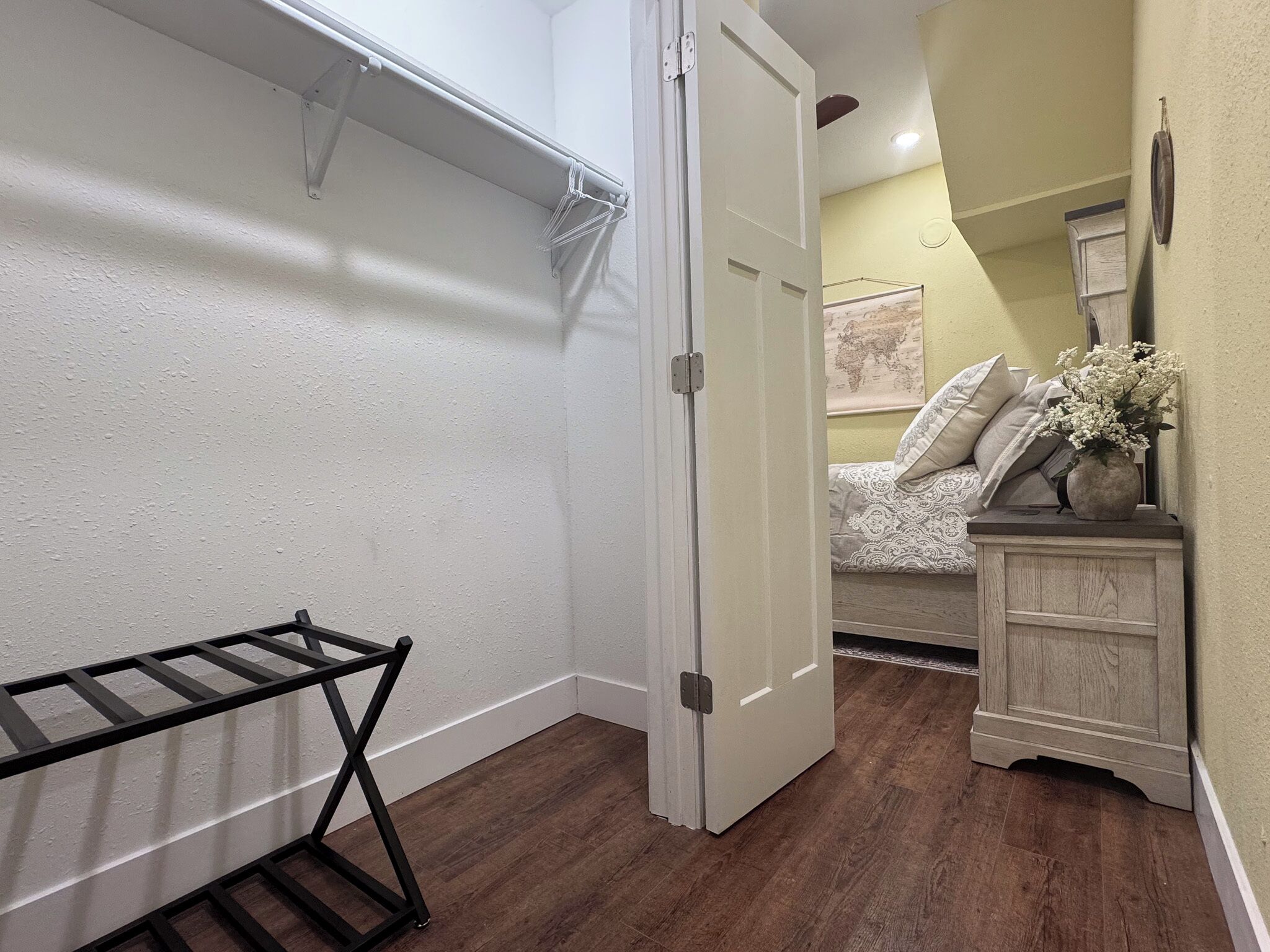 A room with a wooden floor, a white door, a bed with patterned bedding, a dresser, and a wall-mounted map.