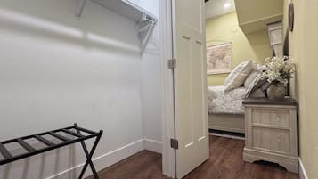 A room with a wooden floor, a white door, a bed with patterned bedding, a dresser, and a wall-mounted map.