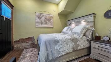 A bedroom with a bed, a nightstand, a clock, a world map on the wall, and a window with blinds.