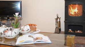Een knusse woonkamer met een open haard, een televisie en een tafel gedekt met theekopjes, een boek en een bord eten.