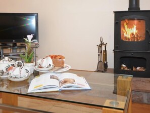 Ein gemütliches Wohnzimmer mit Kamin, Fernseher und einem Tisch, der mit Teetassen, einem Buch und einer Speiseplatte gedeckt ist.