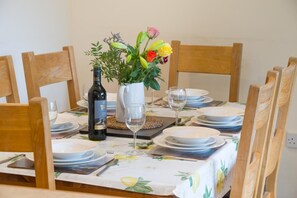 A dining table set with plates, a wine bottle, a vase with flowers, and a glass. - 3 Bed in Crickhowell (oc-tyobr) (Cwmdu)