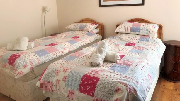 Een kamer met twee eenpersoonsbedden, elk voorzien van een bed met patroon en kussens, een houten hoofdbord, een ingelijste foto aan de muur en een nachtkastje met een lamp.