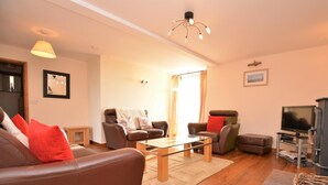 Een woonkamer met een bruine leren bank, twee fauteuils, een glazen salontafel, een televisie en een open haard.