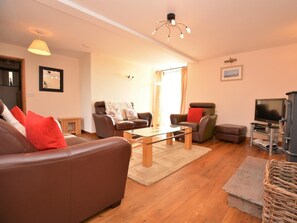 Ein Wohnzimmer mit braunem Ledersofa, zwei Sesseln, einem Glastisch, einem Fernseher und einem Kamin.