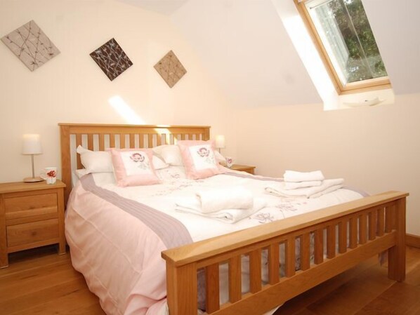 A bedroom with a wooden bed, a nightstand, a bedside table, and a window with a view of trees.