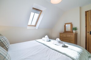 Un dormitorio con una cama, un aparador de madera, un ventanal pequeño y una puerta.