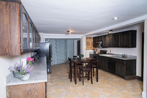 Una cocina con alacenas de madera oscura, encimera de granito, una mesa de comedor con sillas y un refrigerador.