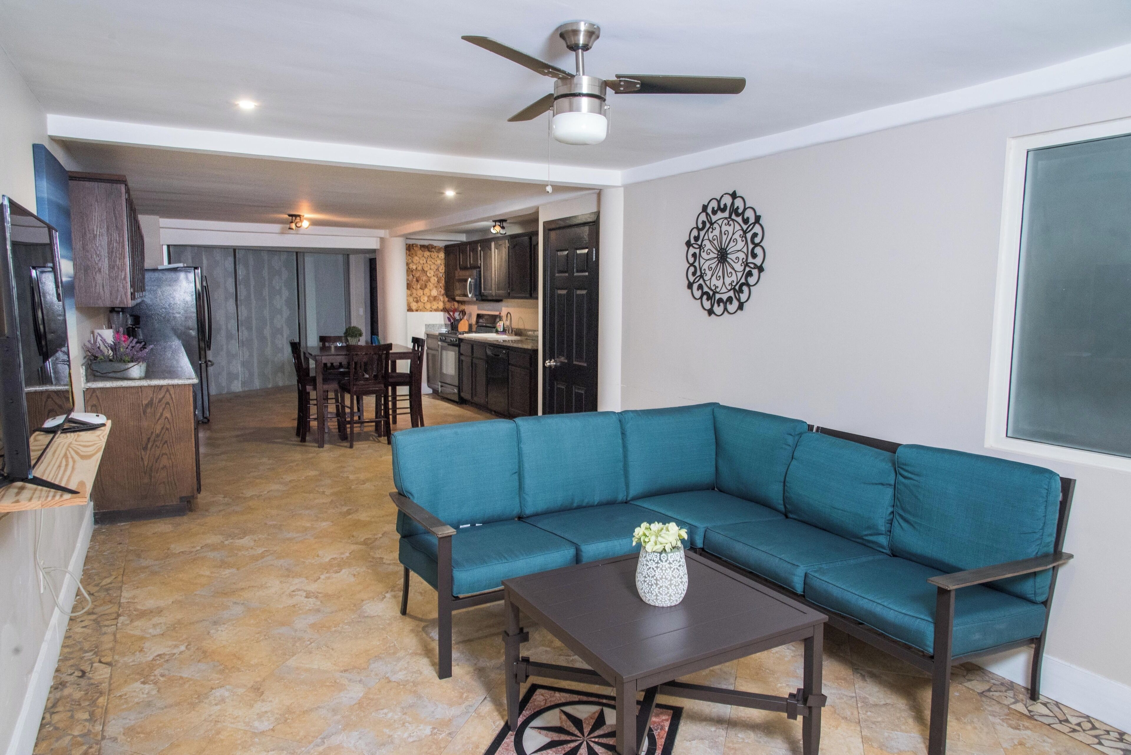 Una sala de estar con un sofá color turquesa, una mesa de centro y un comedor con sillas y una mesa.