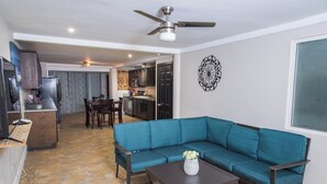 A living room with a teal sofa, a coffee table, and a dining area with chairs and a table. - Oceanfront Escape Breathtaking Sea Views (San Antonio del Mar)