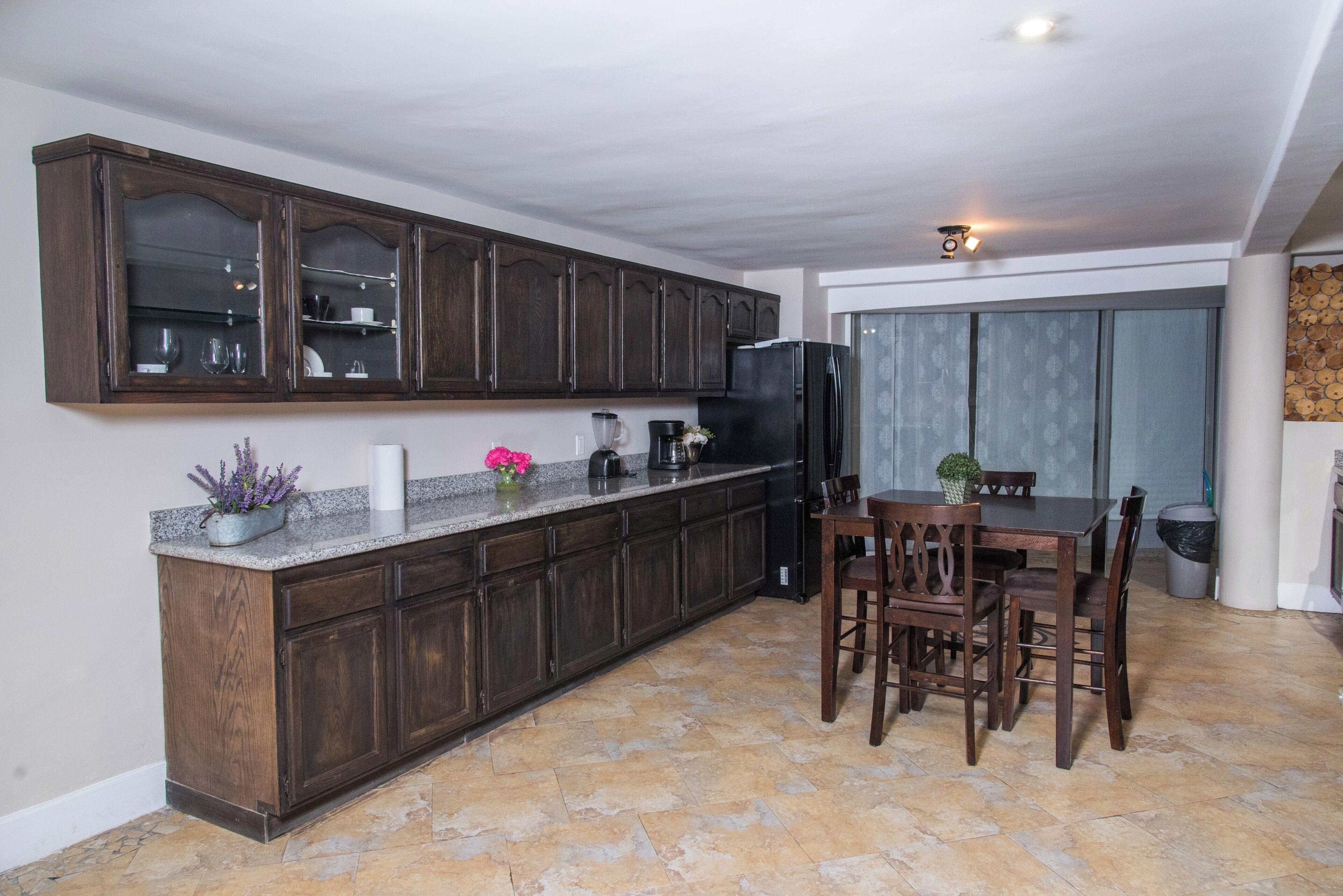 Una cocina con gabinetes de madera oscura, encimera de granito y un comedor con mesa y sillas.