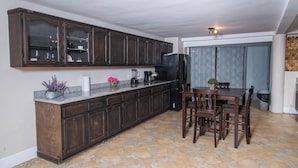 A kitchen with dark wooden cabinets, a granite countertop, and a dining area with a table and chairs. - Oceanfront Escape Breathtaking Sea Views (San Antonio del Mar)