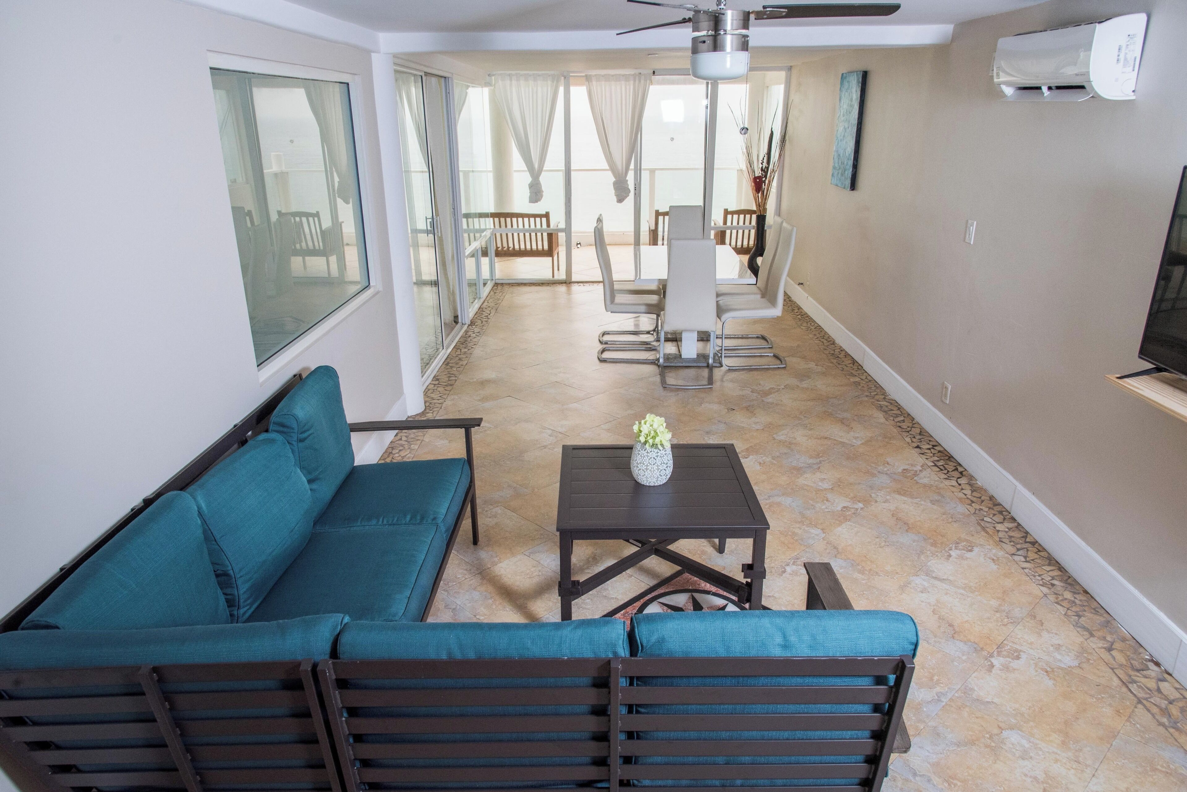 A living room with a sofa, a coffee table, and a TV. There is a dining area in the background with a table and chairs.