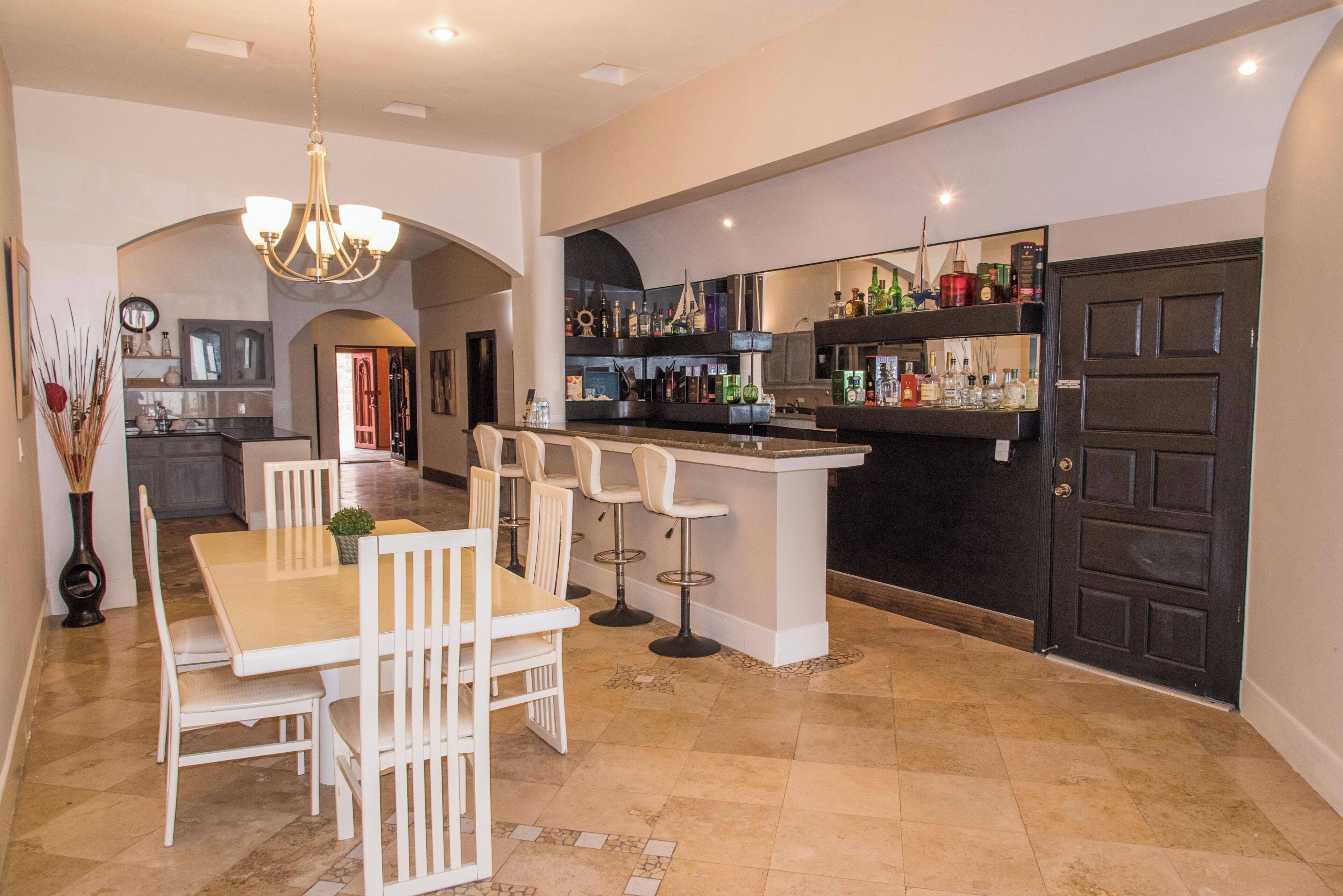 Cocina amplia con comedor, que incluye una barra con taburetes y una variedad de botellas.