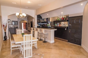 Cocina amplia con comedor, que incluye una barra con taburetes y una variedad de botellas.