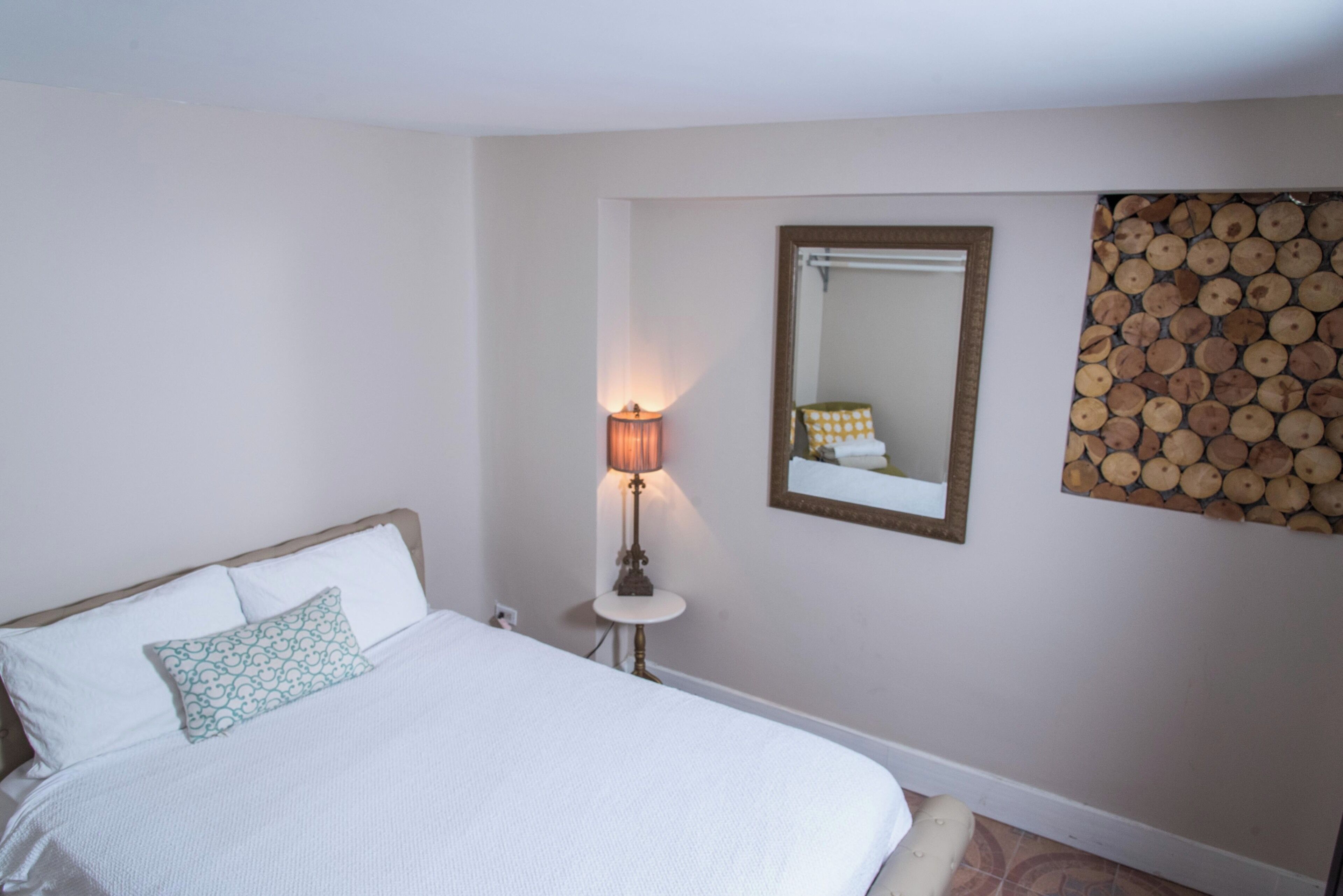 Un dormitorio con cama, mesita de noche con lámpara, espejo y un adorno de leña en la pared.