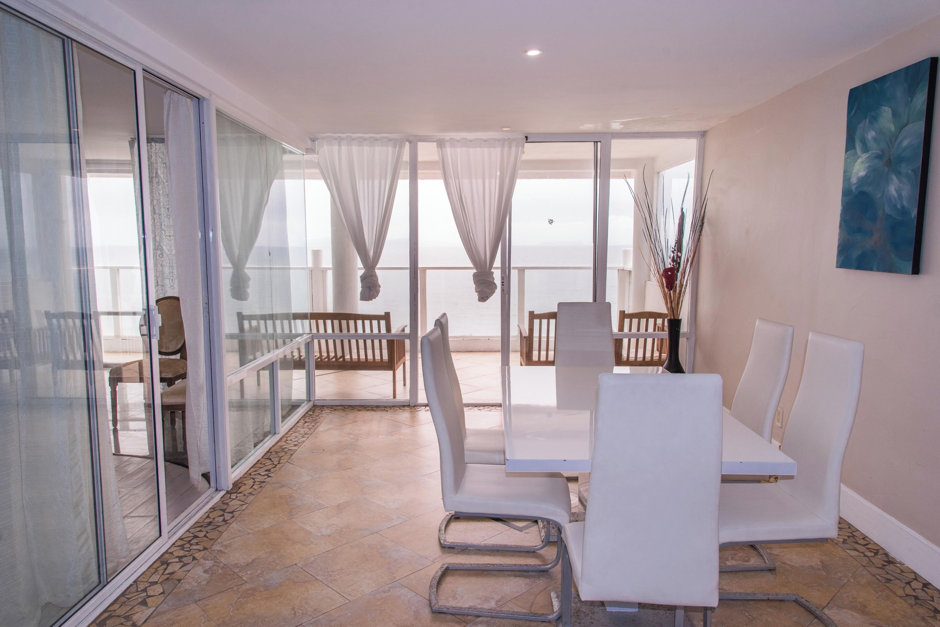 A modern outdoor seating area with a glass balustrade, white furniture, and a view of the sea.