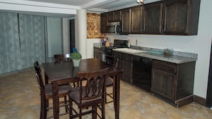 A kitchen with dark wood cabinets, a granite countertop, a built-in microwave, and a dishwasher. There is a dining table with chairs and a potted plant. - Oceanfront Escape Breathtaking Sea Views (San Antonio del Mar)