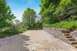 A gravel path leading to a stone wall with a paved area.
