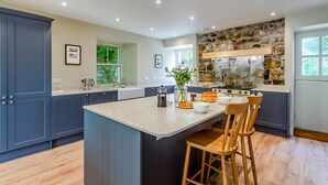 A modern kitchen with a large island, dark blue cabinetry, a stone accent wall, and a view of greenery outside. - 4 Bed in Ardvasar (oc-r43279) (Ardvasar)