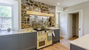 A modern kitchen with a stone wall, built-in oven, and wooden flooring. - 4 Bed in Ardvasar (oc-r43279) (Ardvasar)