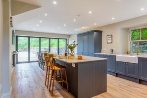A modern kitchen with a central island, bar stools, and a view through large windows.