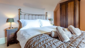 A neatly made bed with a quilted bedspread and two pillows, a bedside table with a lamp, and a wooden wardrobe in a room with peach-colored walls. - 4 Bed in Ardvasar (oc-r43279) (Ardvasar)