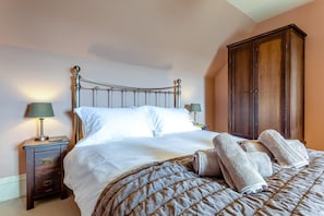 Ein ordentlich gemachtes Bett mit gesteppter Bettdecke und zwei Kissen, ein Nachttisch mit Lampe sowie ein Holzschrank in einem Zimmer mit pfirsichfarbenen Wänden.