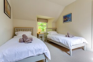 A room with two beds, each with white bedding and rolled towels. There is a window with a view of greenery outside.