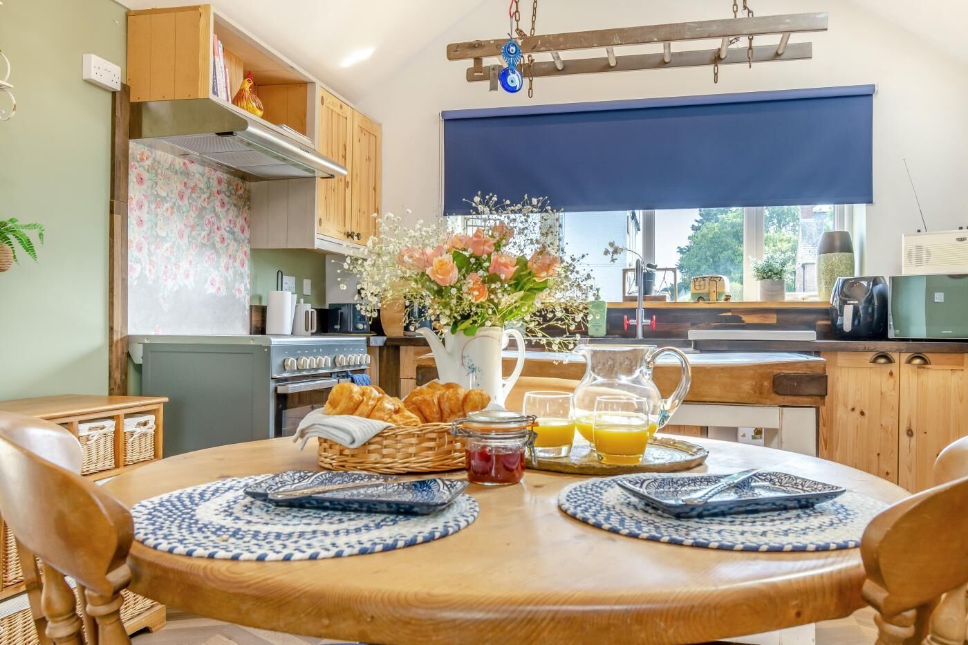 Eine Küche mit Holzausstattung, einem Esstisch mit Platzsets, einer Vase mit Blumen und Frühstücksgebäck.