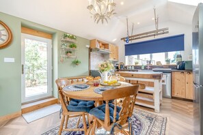 A modern kitchen with wooden cabinets, a dining table with blue cushioned chairs, and a chandelier. - 2 Bed in Partney (oc-v44757) (Partney)