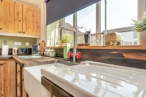 Cozinha com armários de madeira, pia e janela com vista para casas.