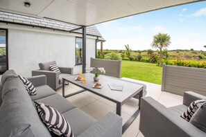 Un'area esterna moderna con un divano, un tavolino e vista su un giardino rigoglioso.