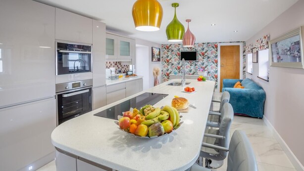 A modern kitchen with a central island, stainless steel appliances, and a colorful backsplash. - 3 Bed in Bryngwran (oc-y44816) (Bodedern)