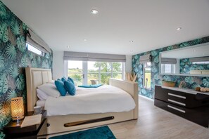 Ein modernes Schlafzimmer mit einem großen Bett, einem Nachttisch, einer Kommode und einem Fenster mit Blick ins Grüne.