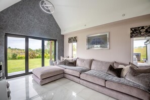 Ein modernes Wohnzimmer mit einem großen Ecksofa, einem Kamin und Blick ins Freie.
