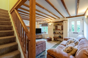 A staircase with wooden balusters leading to a living room with a leather sofa, a television, and a bookshelf. - 4 Bed in Weare Giffard (oc-w44710) (Weare Giffard)
