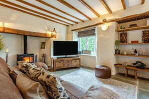 A cozy living room with a fireplace, a flat-screen TV, a sofa, and a bookshelf. - 4 Bed in Weare Giffard (oc-w44710) (Weare Giffard)