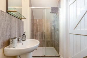 A bathroom with a glass-enclosed shower, a white sink, and a mirror. - 4 Bed in Weare Giffard (oc-w44710) (Weare Giffard)