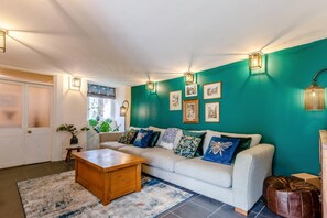 A living room with a sofa, coffee table, and wall-mounted lights. - 4 Bed in Weare Giffard (oc-w44710) (Weare Giffard)
