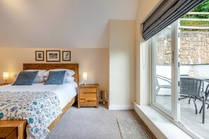 A bedroom with a bed, bedside tables, a window with a view of the outside, and framed pictures on the wall. - 4 Bed in Weare Giffard (oc-w44710) (Weare Giffard)