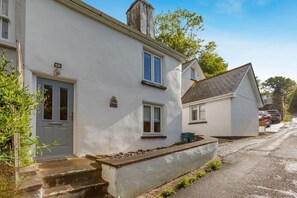 A two-story house with a grey door, a small porch, and a visible chimney. - 4 Bed in Weare Giffard (oc-w44710) (Weare Giffard)