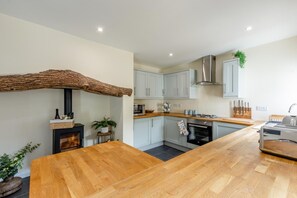 A modern kitchen with a central island, built-in appliances, and a rustic wooden beam. - 4 Bed in Weare Giffard (oc-w44710) (Weare Giffard)