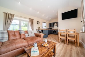Ein gemütliches Wohnzimmer mit einem braunen Ledersofa, einem Couchtisch aus Holz mit einem Buch und einer Tasse, sowie einem Essbereich mit Holztisch und Stühlen.