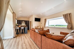 Ein modernes Wohnzimmer mit einer Couch, einem Essbereich mit Stühlen, einer Küche mit Bar und einem großen Fenster mit Aussicht.