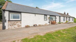A white building with a grey roof, a stone foundation, and a paved driveway. - 2 Bed in Kirkmahoe (oc-h44227) (Dumfries)