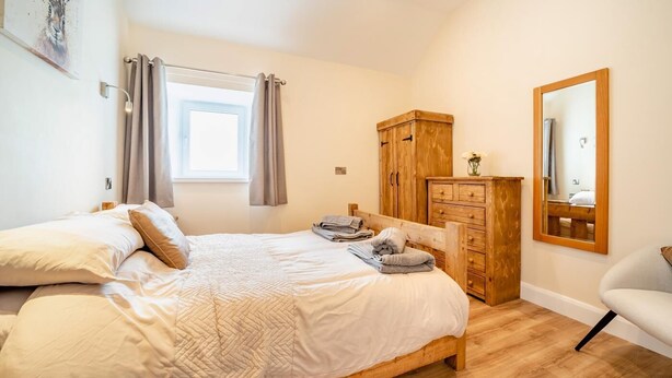 A bedroom with a bed, a wooden wardrobe, a mirror, and a window with curtains. - 2 Bed in Kirkmahoe (oc-h44227) (Dumfries)