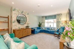 A living room with a blue sectional sofa, a wooden cabinet, and a large mirror on the wall. - 5 Bed in Pocklington (oc-m45222) (Pocklington)